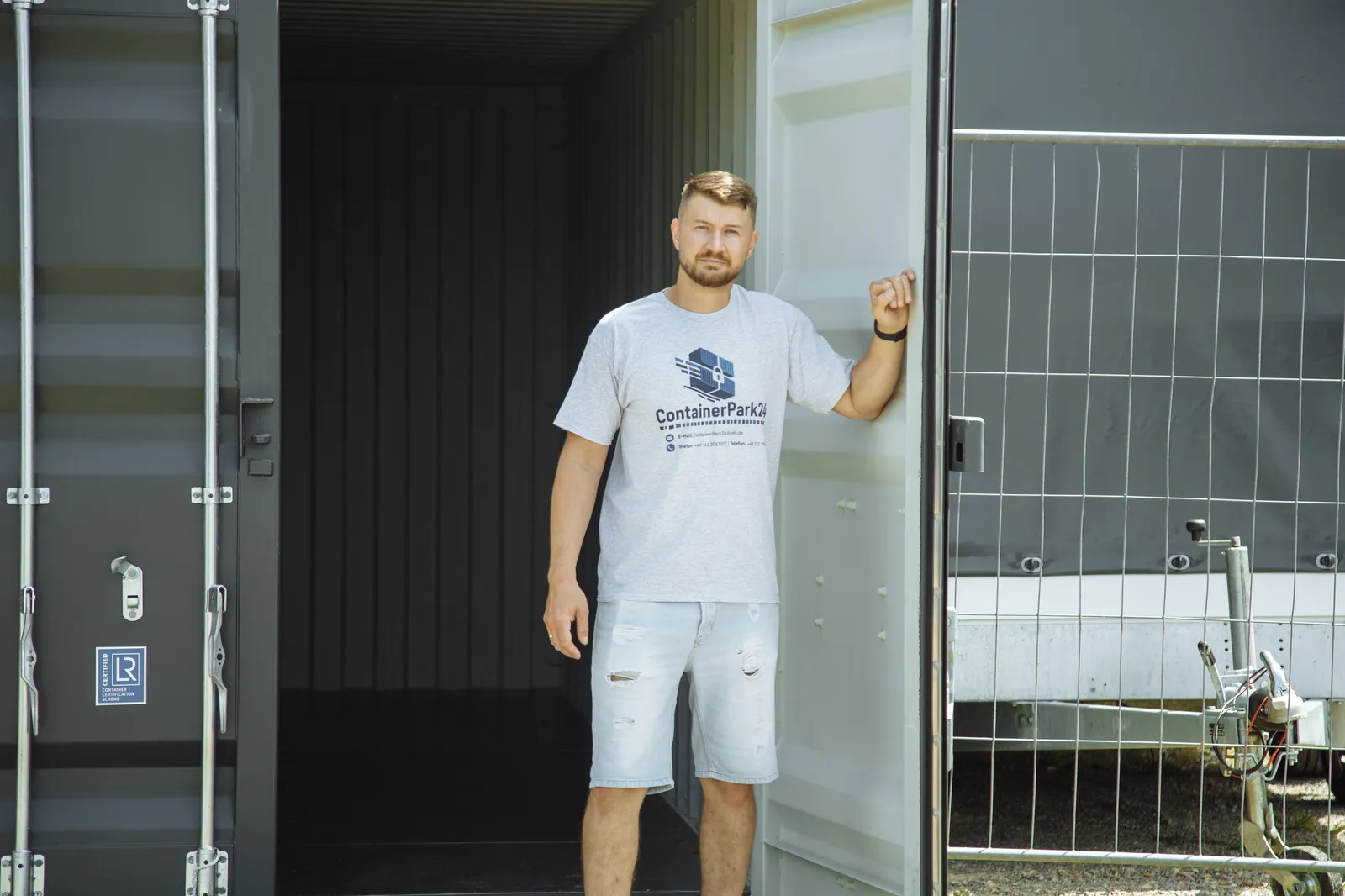 Mitarbeiter lehnt am Containertor und blickt in die Kamera.
