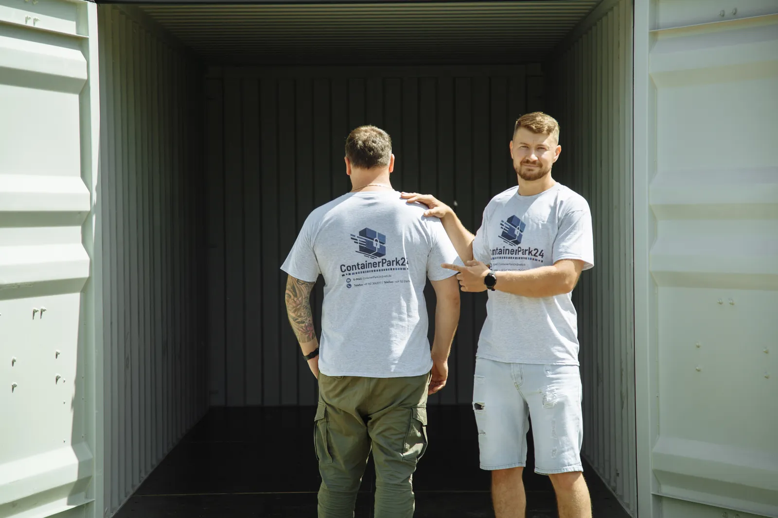 Zwei Mitarbeiter mit ContainerPark24-Shirts vor einem Container.