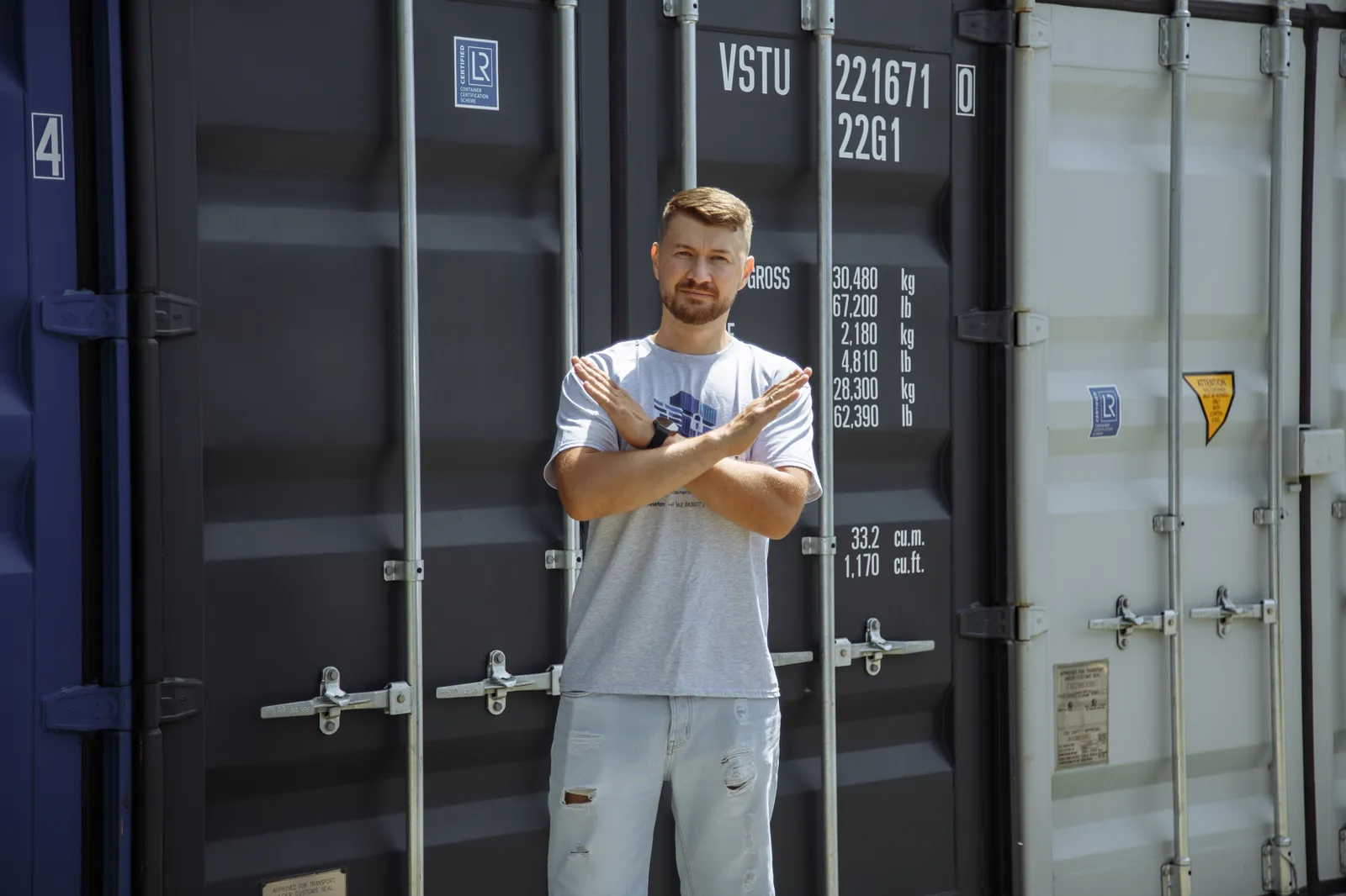 Mitarbeiter vor einem Container, verschränkt selbstbewusst die Arme.